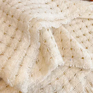 Detailopname van een crème witte wollen sjaal met opengewerkte textuur en franjes