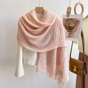 Detail van roze gebreide wollen sjaal met wafeltextuur en franjes op witte blazer