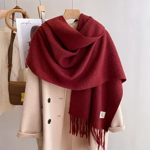 Burgundy solid color thick scarf with tassel trim and label on beige wool coat