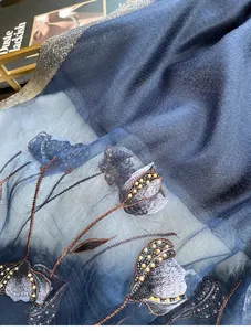 Close-up of blue silk blend scarf with floral embroidery, beadwork and gold silk edges