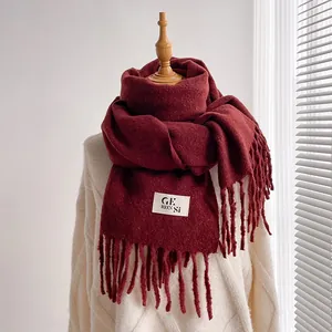 Detail of burgundy scarf with long tassels and logo label worn on a knit sweater