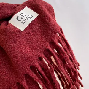 Detail of dark red knit scarf showing thick texture, tassels, and square fabric brand label