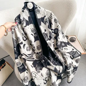 Detail of a thick black and white panda print scarf with a camellia brooch on a chair