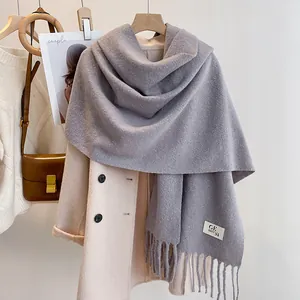 Detailed close-up of light gray knit scarf with fringe and brand label on winter coat