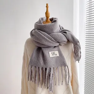 Close-up of dark grey thick fringe scarf with brand label on a wooden hanger model