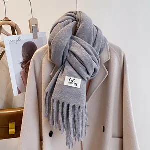 Close-up of grey knit scarf with fringe and logo tag styled on a wool coat