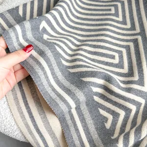 Nahaufnahme von dickem Strickschal mit grau-weißem Labyrintmuster und weicher Textur