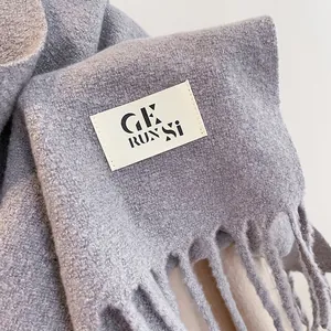 Close-up of soft knitted scarf texture with fringe details and a minimalist brand tag