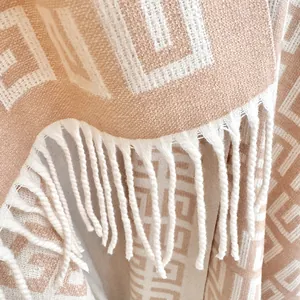 Macro detail of beige cashmere-feel scarf featuring geometric patterns and white tassels