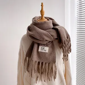 Detail of coffee brown scarf featuring fringe edges and a minimalist brand label on fabric