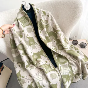 Detail of soft green and cream scarf with bear pattern draped on a textured chair