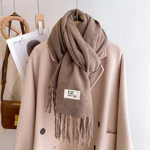 Close-up of thick dark coffee scarf with fringe detail and label on a wool coat