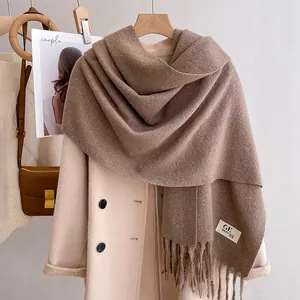 Detail of taupe thick scarf with long tassels and woven label on a beige coat