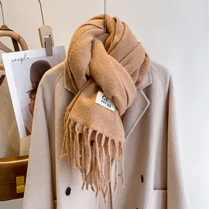 Detail of camel fringe scarf showing soft knit texture and woven brand label on wool coat
