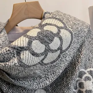 Close-up of grey tweed scarf featuring white camellia knit pattern and elegant texture