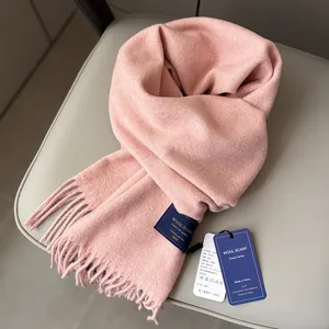 Pink wool scarf with tassel trim and woven label on a light grey leather chair