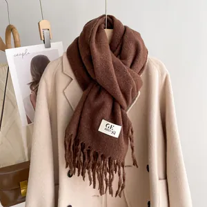 Detail shot of brown plush scarf fringe and brand tag on a beige wool coat