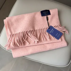 Detail of light pink wool scarf showing soft texture, fringe edges and label on leather seat