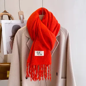 Close-up of bright orange knitted scarf with fringes and logo patch on wool coat