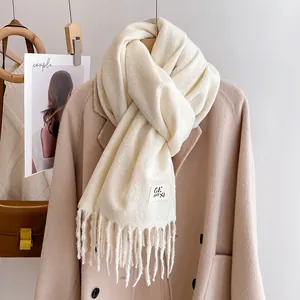 Close-up of cream knit scarf featuring soft texture, long tassels, and a minimalist fabric label
