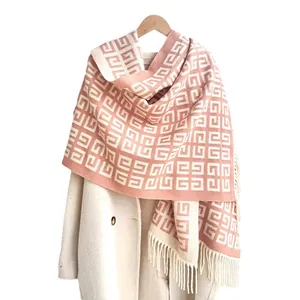 Pink and white G-pattern knit scarf with tassels styled on a white coat and hanger