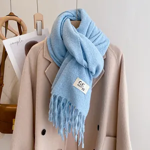 Detail of light blue knitted scarf featuring long tassel fringe and soft wool-like texture