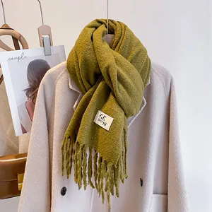 Detail of mustard yellow knit scarf with fringe and label on a beige wool coat