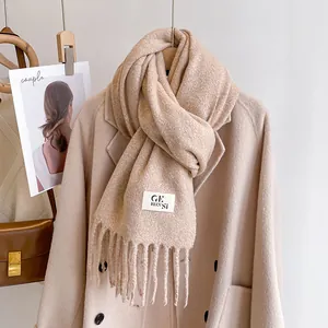 Detail of beige knitted scarf with soft fringe edges and branded woven label
