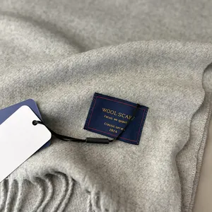 Close-up of light grey wool scarf showing soft fringe details and a woven brand label