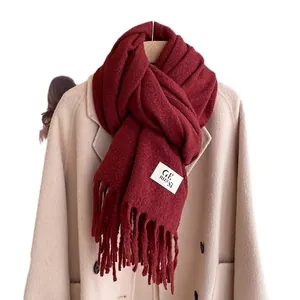 Deep red thick knit scarf with tassels and brand label on a beige wool coat