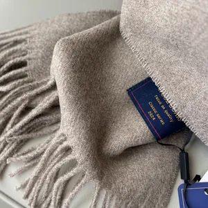 Detail of oatmeal wool scarf texture with elegant tassels and stitched embroidered label