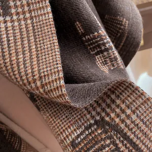 Macro shot of thick houndstooth and plaid patterned wool scarf with H embroidery