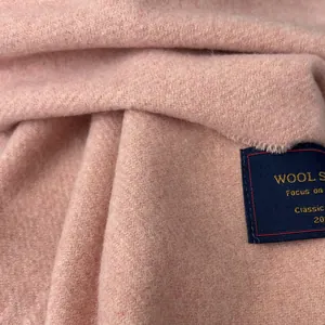 Macro shot of light pink wool scarf fabric showing soft diagonal weave texture and logo label
