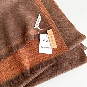 Detailed close-up of brown and orange knit scarf with soft fringe and brand tag