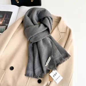 Detail of grey cashmere scarf with fringe tassels on a beige coat with brand tag