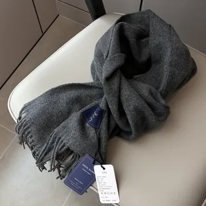 Close-up of charcoal gray wool scarf texture with fringe details and product tags