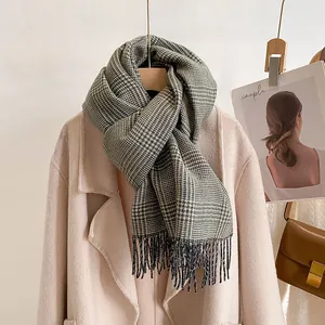 Close-up of gray and black houndstooth plaid scarf with fringe details on beige coat