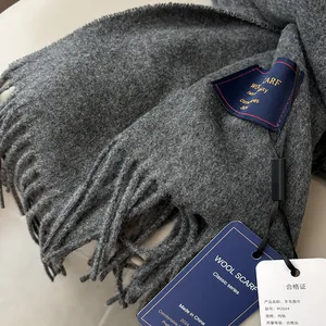 Detailed view of dark grey wool scarf texture with elegant tassels and woven label