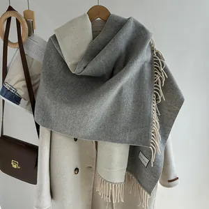 Gray and white double-sided wool blend scarf with fringe on a beige coat