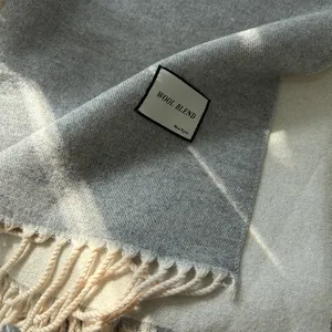 Close-up of wool blend scarf texture showing grey plaid pattern and tassel fringe detail