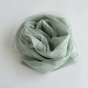 Macro shot of sage green silk scarf showing soft translucent texture and fine pleats