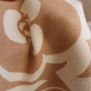 Macro shot of camellia jacquard pattern on a soft camel and cream cashmere-feel scarf