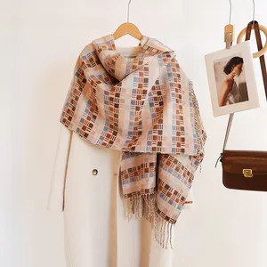 Close-up of winter plaid scarf with tassels on beige wool coat hanging on wooden hanger