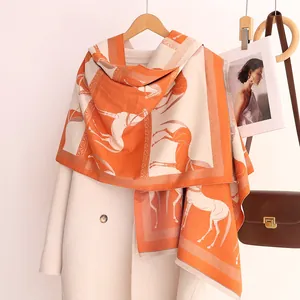 Détail de l'écharpe en cachemire à motif de cheval et pompons oranges sur un manteau