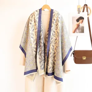 Detail of paisley pashmina shawl with blue borders and fringe on a wooden hanger