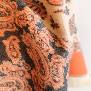 Close-up of paisley print cashmere-feel scarf texture with fringe detail in warm tones