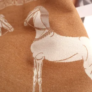 Gros plan détaillé du motif cheval jacquard sur une écharpe douce couleur camel