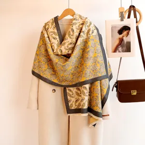 Detail of paisley ginger yellow cashmere-feel shawl with tassels over beige wool coat