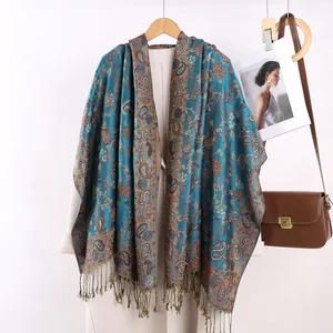 Dettaglio di scialle vintage con motivo paisley e nappe sopra un cappotto bianco