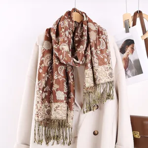 Dettaglio di sciarpa marrone con motivo paisley e frange, abbinata a cappotto bianco